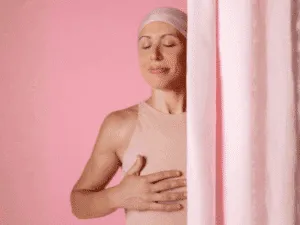 Ricostruzione areolare - il ruolo del tatuaggio 3D del capezzolo Donna con bandana rosa che appoggia la mano sul petto, simbolo di forza dopo un percorso oncologico.