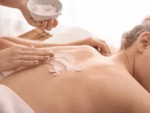 Trattamento di esfoliazione corpo professionale con scrub applicato sulla schiena in centro estetico