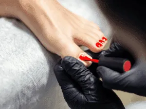 Applicazione di smalto rosso durante pedicure estetica professionale.
