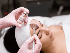 Trattamento viso PRX-T33 non invasivo. Primo piano estetista con guanti rosa che applica il trattamento biorivitalizzante PRX-T33 sulla fronte.