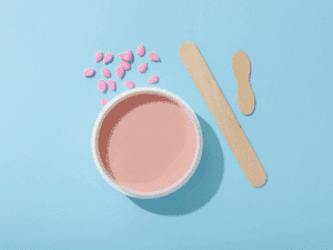 Contenitore con cera brasiliana rosa fusa e spatole di legno per l’applicazione della ceretta.