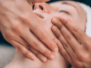 Massaggio viso lifting eseguito su una donna mentre si concentrano sulla mandibola e il collo, con mani che applicano una pressione delicata.