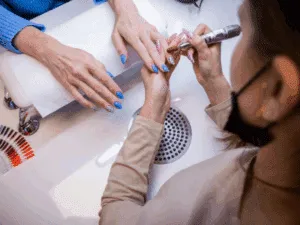Onicotecnica che utilizza la fresa per unghie su una cliente durante una manicure professionale.