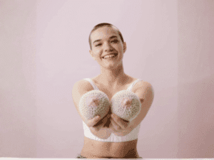 Dermopigmentazione seno: una soluzione sicura e personalizzata Giovane donna sorridente che mostra due seni lavorati all’uncinetto.