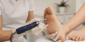 Estetista professionista esegue una dry pedicure su piede asciutto con fresa elettrica in ambiente moderno e pulito.