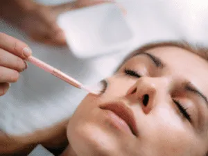 Donna distesa durante l’applicazione di un peeling enzimatico viso con pennello professionale.