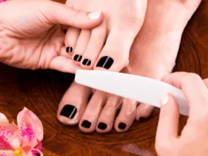 Estetista che lima le unghie dei piedi con smalto nero durante una pedicure estetica.
