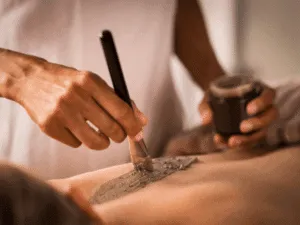 Estetista che applica fango per il corpo con un pennello sulla schiena durante un trattamento di fanghi riducenti e anticellulite.