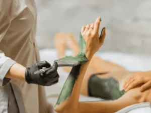 Operatrice estetica stende fango per il corpo su braccio e addome in una sessione di fangoterapia con fanghi anticellulite.
