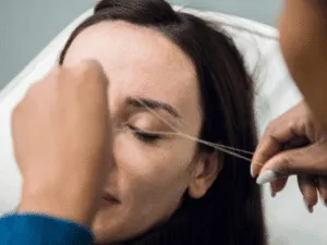 Epilazione con filo su sopracciglia in un trattamento estetico professionale.