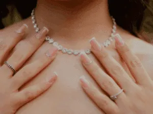 Mani femminili con french manicure elegante e squadrata, abbinate a collana e anelli luminosi.