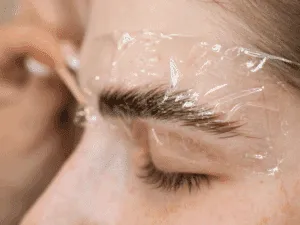 fase di posa della laminazione sopracciglia nel trattamento brow lift Fase della laminazione sopracciglia con copertura protettiva per il fissaggio