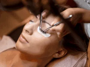 Estensioni ciglia su cliente Lash maker che applica estensioni ciglia a una cliente durante un trattamento di allungamento professionale.