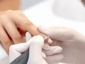 Operatrice con guanti bianchi che utilizza la fresa per pulire la lamina ungueale durante la manicure russa a secco.
