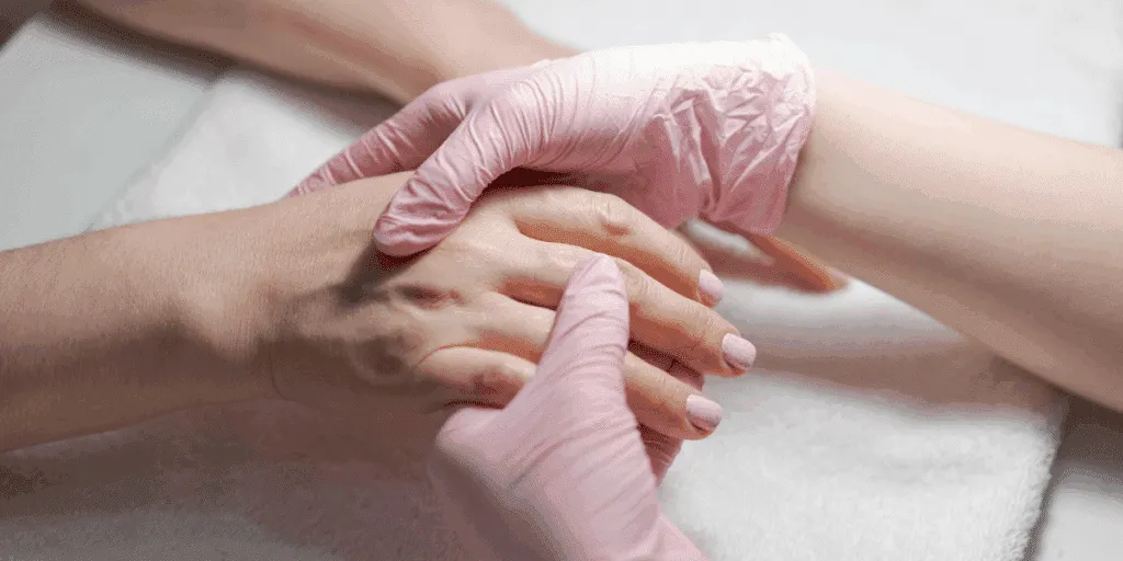Manicure curativa professionale con estetista che tratta la mano della cliente indossando guanti rosa