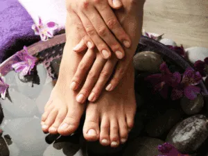 Manicure e pedicure spa con mani e piedi curati immersi in acqua con fiori e pietre naturali.