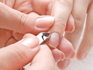 Primo piano della rimozione precisa delle cuticole con tronchesina durante una manicure estetica.
