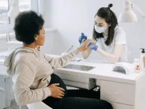 Estetista professionista che esegue una manicure curativa a una cliente seduta al tavolo estetico