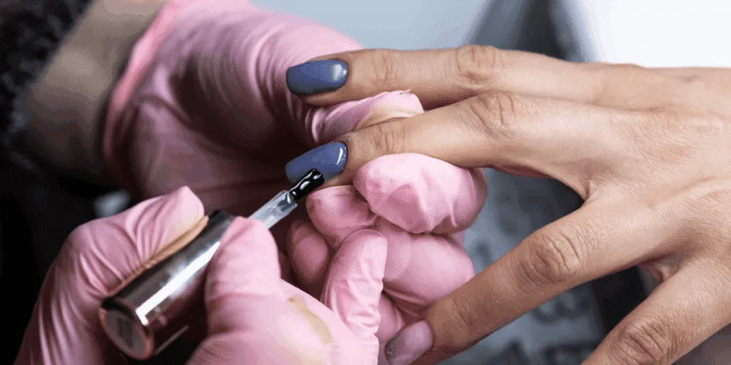 Applicazione dello smalto semipermanente su unghie delle mani da parte di un’estetista con guanti rosa