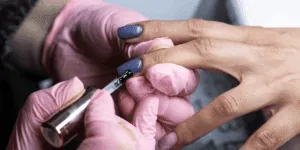 Applicazione dello smalto semipermanente su unghie delle mani da parte di un’estetista con guanti rosa