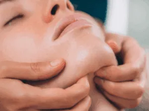 Donna che riceve un massaggio lifting sotto il mento per stimolare i muscoli e definire l'ovale del viso.