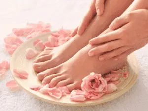 Piedi immersi in una ciotola con petali di rosa durante un trattamento di pedicure estetico