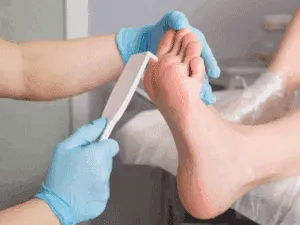 Operatore estetico con guanti azzurri utilizza spatola su piede asciutto durante dry pedicure.