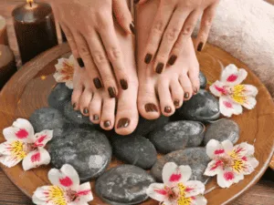 Pedicure e manicure spa con smalto marrone e trattamento rilassante su pietre calde e fiori.