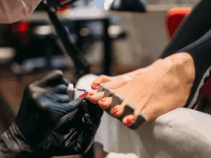 estetista applica smalto semipermanente rosso durante una pedicure professionale