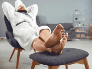 uomo rilassato con accappatoio si prende cura dei piedi a casa