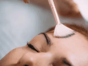 Estetista applica una soluzione esfoliante sulla fronte di una cliente durante un trattamento.