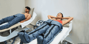 Uomo e donna sdraiati durante una seduta di pressoterapia in centro estetico con gambali pressoterapici per migliorare il drenaggio linfatico, i benefici della pressoterapia e la circolazione delle gambe.