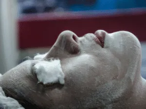 Posa della maschera purificante durante la pulizia viso Persona sdraiata con maschera purificante e cotoni sugli occhi durante un trattamento viso rilassante in istituto estetico.