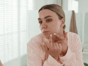 Donna che osserva i brufoli sul viso allo specchio dopo la pulizia del viso