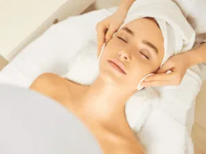 Tonificazione del viso con pulizia professionale Cliente distesa mentre un’operatrice estetica tonifica e deterge il viso utilizzando dischetti durante il trattamento skincare.