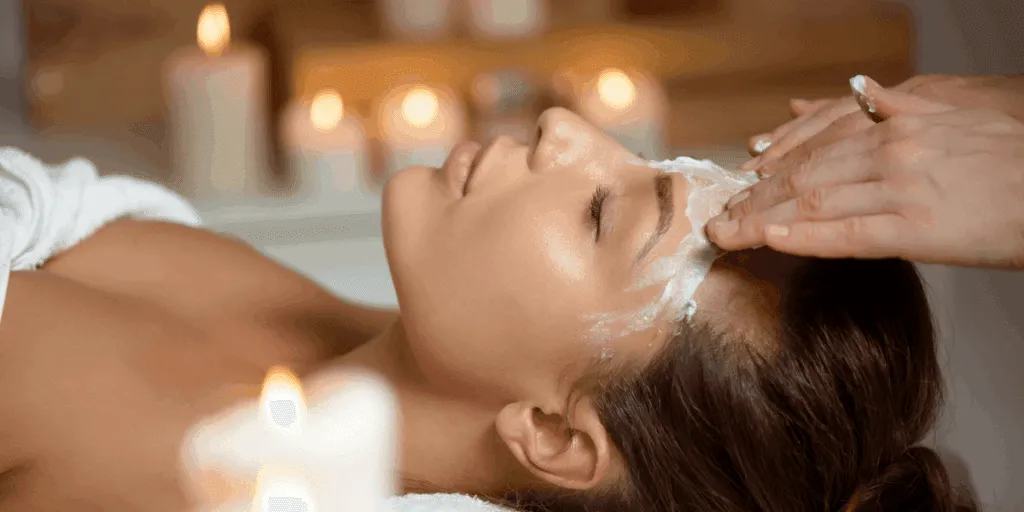 Donna sdraiata in un centro estetico mentre un’operatrice applica una crema detergente sul viso durante una pulizia viso professionale.