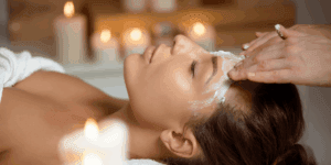 Donna sdraiata in un centro estetico mentre un’operatrice applica una crema detergente sul viso durante una pulizia viso professionale.