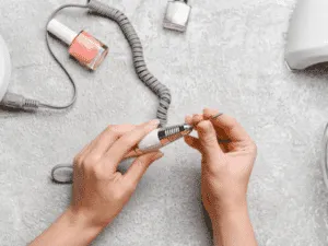 Mani che impugnano una fresa elettrica per unghie insieme a smalti e strumenti per manicure russa.