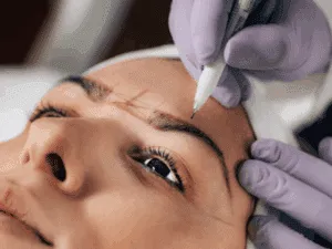 Operatrice estetica che disegna linee guida prima del trattamento di trucco semipermanente sopracciglia.