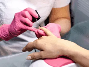Applicazione dello smalto semipermanente su unghie delle mani da parte di un’estetista con guanti rosa