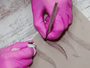 Esercitazione su pelle sintetica della tecnica microblading, con penna manuale e pigmento per tracciare sopracciglia realistiche.