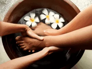 Trattamento piedi rilassante con pediluvio e fiori profumati in una ciotola di legno.