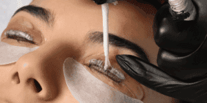 Applicazione del prodotto durante la laminazione ciglia su cliente distesa, con patch protettivi e operatrice che esegue il trattamento professionale.