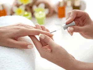 Estetista che applica lo smalto su unghie curate durante una manicure estetica professionale.