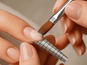 Applicazione del gel acrilico su unghia naturale con forma guida durante la ricostruzione professionale.
