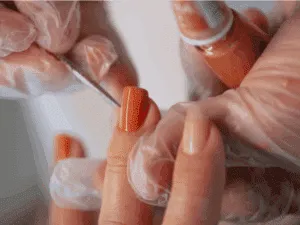 Applicazione di smalto semipermanente color arancio durante una manicure professionale